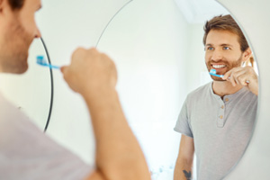 Handsome man brushing his teeth in front of bathroom mirror