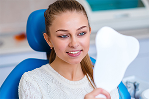 Woman looking at smile in mirror after porcelain veneers treatment