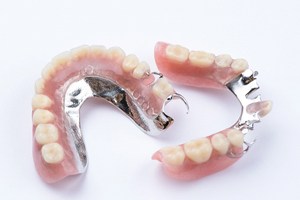Two partial dentures with metal attachments against neutral background
