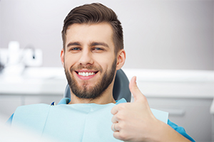 Man in dnetal chair giving thumbs up after emergency dentistry