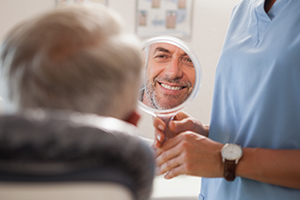 Man looking at smile in mirror after dental implant tooth replacement