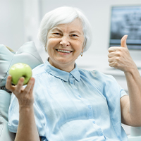 Woman holding an apple and smiling after replacing all missing teeth