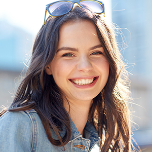 Woman with sunglasses on head smiling after orthodontic treatment