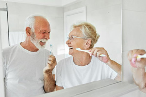 Older couple brushing their teeth in front of bathroom mirror