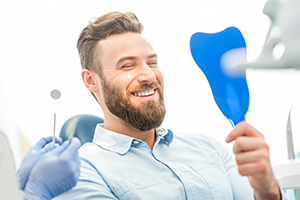 Man checking smile in blue mirror after full mouth reconstruction