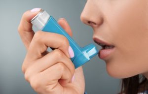 Woman with asthma bringing inhaler to her mouth