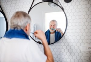 Senior man brushing teeth while adjusting to implant dentures
