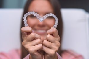 Woman holding aligners, enjoying the benefits of Invisalign after braces in Needham