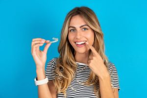 Woman holding Invisalign aligner, pointing at her teeth