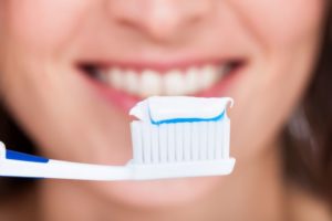 Toothbrush and toothpaste in foreground, woman’s smile in background