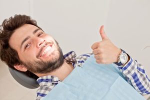 Dental patient reclined in treatment chair, making thumbs up gesture